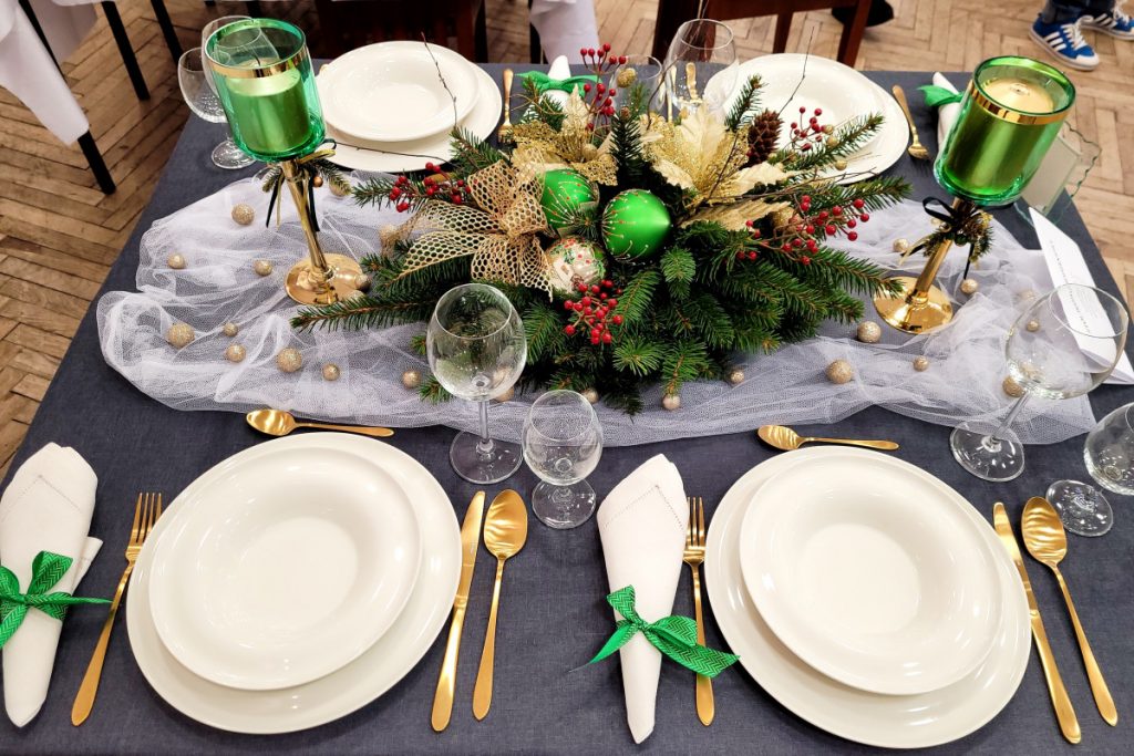 Zdjęcie - II miejsce. Szary obrus , białe serwetki i talerze, złote sztućce, zielone świeczniki, po środku stroik ze świerku z dekoracją zielono-złoto- czerwoną